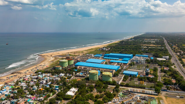 Aerial view of the desalination plant with blue-roofed industrial buildings and large storage tanks situated along the sandy coastline in India.