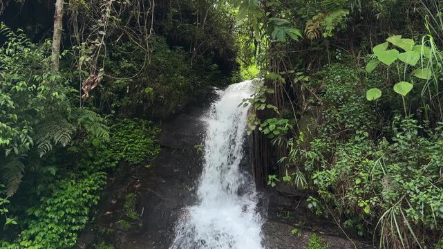 A detailed, frame-filling top shot showcasing the dynamic abstract motion of fresh mountain water splitting and splashing over dark rocky layers at the crest of a natural waterfall.