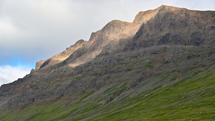 Dramatic view of lush green mountains in the Westfjords of Iceland, with sunlight casting striking rays across the slopes beneath a peaceful sky. © Asanee
