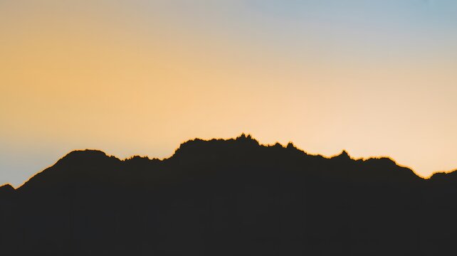Black silhouette of rugged mountain peaks set against a soft gradient warm orange sunset sky background