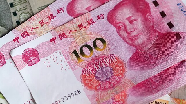 Chinese one hundred yuan (CNY) or renminbi (RMB) bills are placed on top of Indian rupee (INR) notes of difterent denomination. Concept of exchange rate, global finance, and international economy.