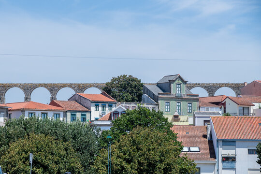 Historic stone aqueduct and red tiled roofs of an ancient town framed by carved granite finials under a clear blue sky.