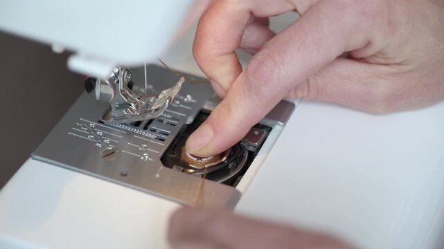 Seamstress hands inserting bobbin into sewing machine. Close-up of a tailor's hands carefully placing a threaded bobbin into the compartment of a sewing machine