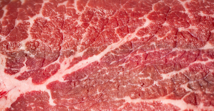 Raw beef texture with natural fat marbling. Raw beef macro background in pink tones. Detailed raw beef surface with muscle fibers. Close-up raw beef forms a food background.