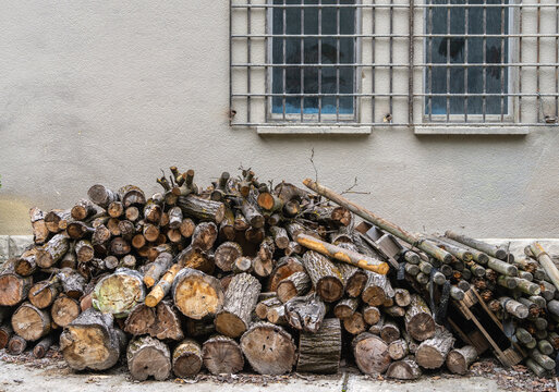 Haufen gelagerter Holzschete und Baumst&auml;mme, die lose vor einer verputzten mit vergittertem Fenster aufgeschichtet sind, Brandenburg, Deutschland
