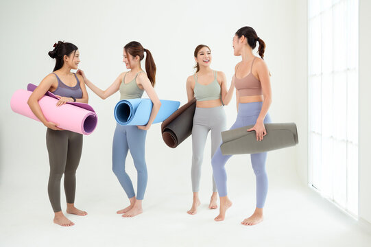 Four Women in a Yoga Class Prepare With Mats and Props on a White Background