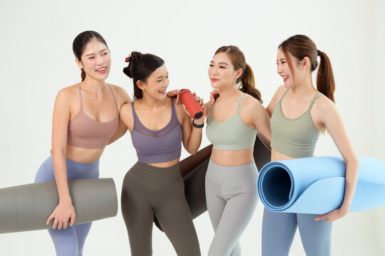 Four Women in a Yoga Class Prepare With Mats and Props on a White Background