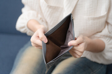 Financial hardship concept. Person showing an empty wallet at home, symbolizing money shortage,...