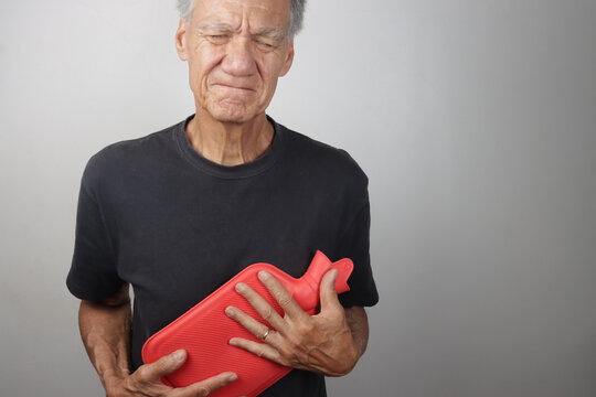 Older Man Applying a Hot Water Bottle on his stomach for pain relief  