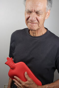 Older Man Applying a Hot Water Bottle on his stomach for pain relief  