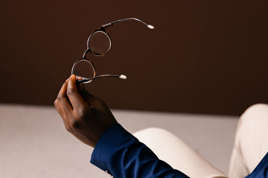 Hand Holding Round Glasses Over Neutral Brown Background
