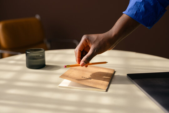 Hand Reaching for Pencil Over Notebook on Office Desk