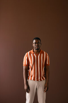 Young Man in Striped T-Shirt Standing Against Brown Background