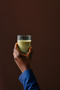Hand Holding Glass Of Green Smoothie Against Brown Background