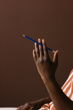 Hand Holding Blue Pencil Over Brown Background 