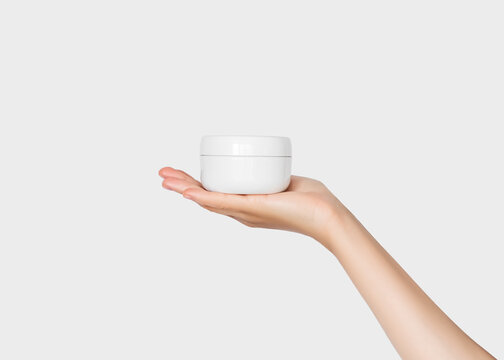 Hand holding a jar of cosmetic cream on a white background. Beauty product concept