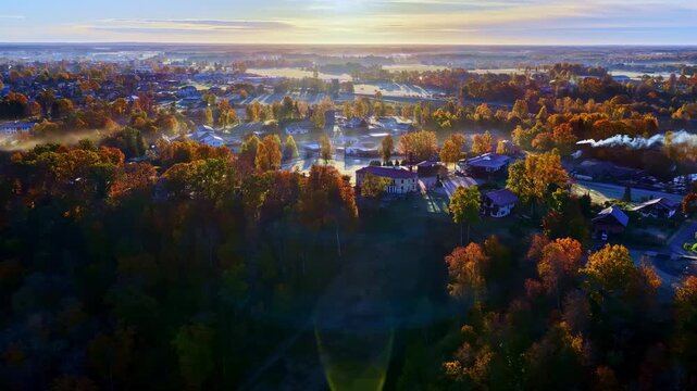 Aerial view of Sigulda Municipality, Latvia, featuring lush autumn-colored forests, scattered buildings, and soft morning light.
