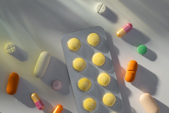 Assortment of colorful pills and blister pack scattered on white table