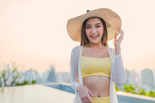 Portrait of cheerful smiling young woman wearing sun hat enjoying golden hour sunset at luxury rooftop, radiating joyful optimism, vitality, happiness, freedom, and vacation vibes.