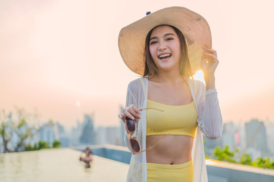 Portrait of cheerful smiling young woman wearing sun hat enjoying golden hour sunset at luxury rooftop, radiating joyful optimism, vitality, happiness, freedom, and vacation vibes.