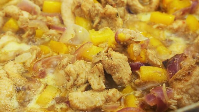 In a deep cast-iron skillet, onions and chicken simmer in a sauce with spices and pepper. Medium shot.
