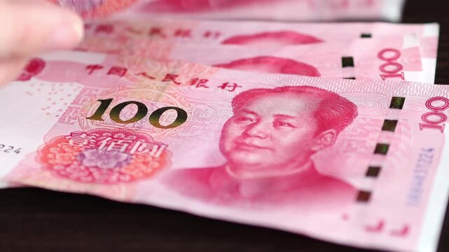 Woman's hands counting Chinese 100 yuan (CNY) or renminbi (RMB) notes by placing bills on a brown table. Chinese cash money. Real time video.	
