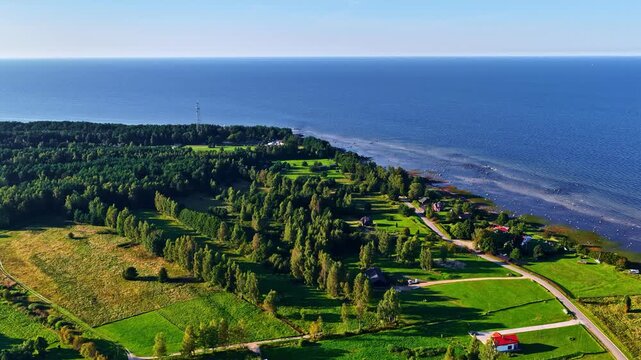 Aerial view of the coastal landscape of Engure featuring lush green fields, dense forests, and a road running along the Baltic Sea coastline in Engure, Tukums Municipality, Latvia.
