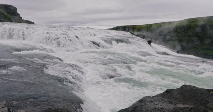 Powerful Gullfoss waterfall cascading through a dramatic canyon in southwest Iceland, with glacial water rushing over multiple rocky tiers and mist rising from the Hv&iacute;t&aacute; River.