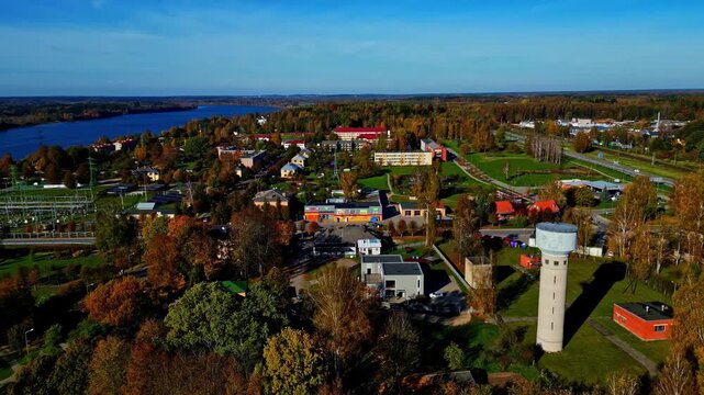 Aerial view of the town of Kegums featuring the prominent water tower, surrounding autumn foliage, and the nearby river in Kegums, Ogres novads, Latvia.