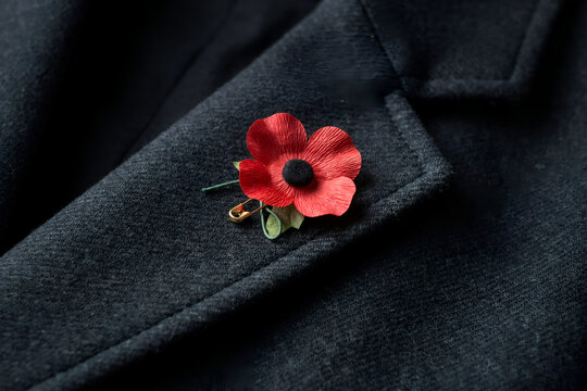 Red poppy lapel pin on charcoal wool coat during remembrance day with soft focus