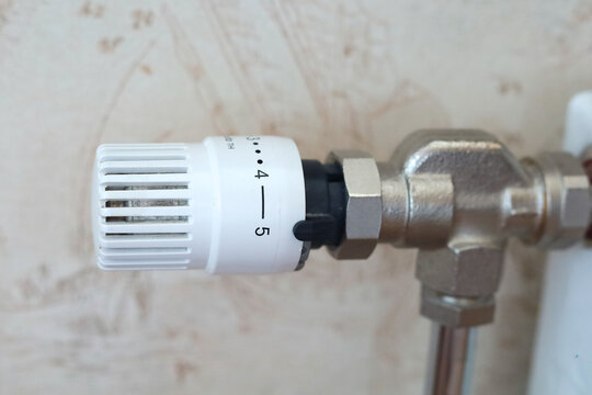 Numbered thermostatic radiator valve is set on a metal heating pipe for temperature adjustment. Concept of heating control, energy saving, household efficiency and indoor comfort.