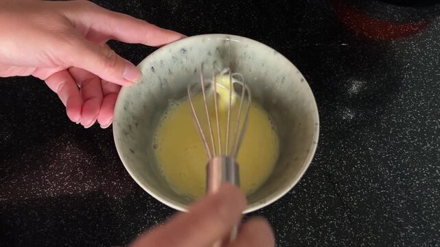 Female hands slowly whisk raw eggs in a ceramic bowl from above, showing careful food preparation with realistic movement and natural kitchen sound. High quality FullHD footage