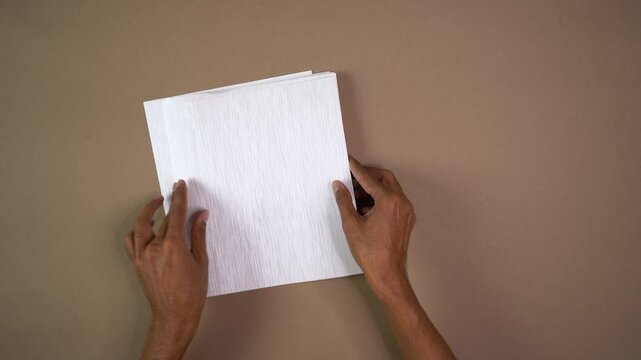 Top-down view of hands fanning out stack of textured white paper sheets