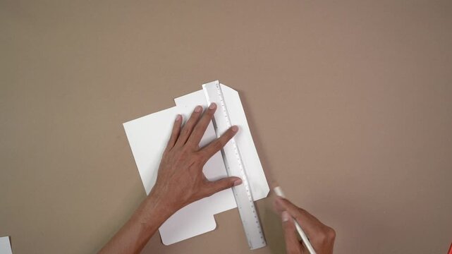 Top-down view of crafter drawing straight line on white paper template for DIY window envelope