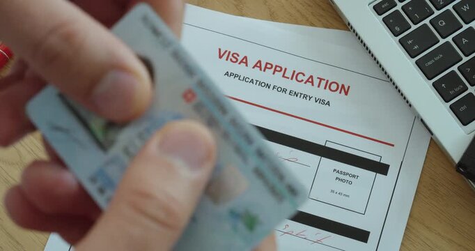 Close-up of a person holding a passport over a visa application form, representing immigration, international travel, entry permits and visa processing.