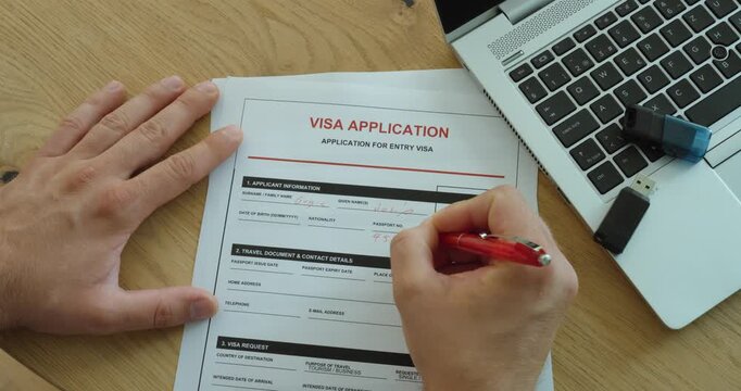 Close-up of a person completing a visa application form at a desk with a laptop, representing immigration, travel authorization and visa processing.