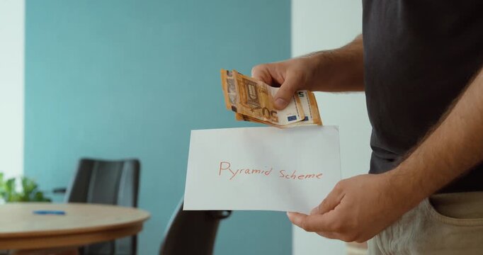 Person holding cash and a pyramid scheme sign, representing investment fraud, financial scams, deceptive business practices and illegal money schemes.