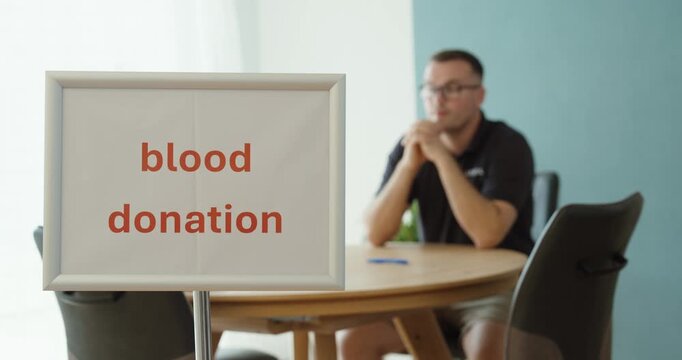 Man sitting and waiting next to a blood donation sign, representing voluntary blood donation, healthcare, donor registration and lifesaving medical support.