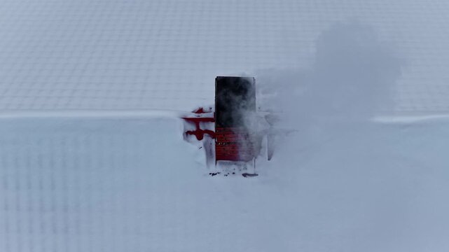 Aerial view of a snow-covered roof with a chimney emitting smoke during a winter day in Latvia.