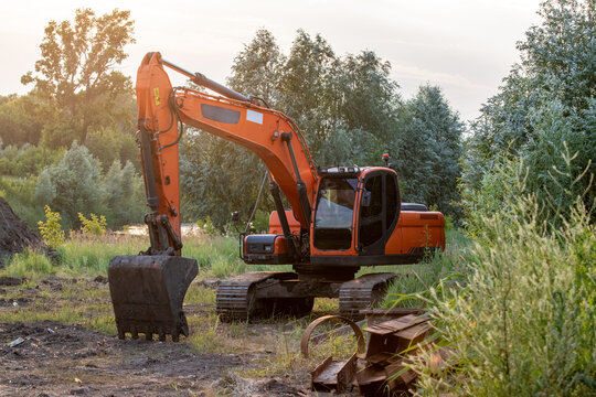 Orange crawler excavator machine parked outdoors near trees