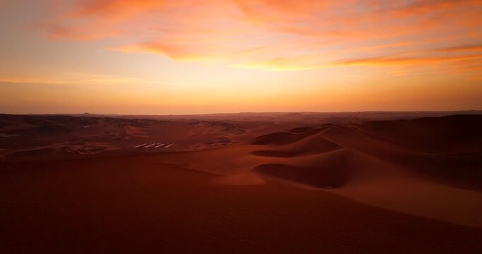Drone flying over rolling sand dunes in Huacachina desert under orange sunset sky in Ica, Peru. Aerial forward, copy space