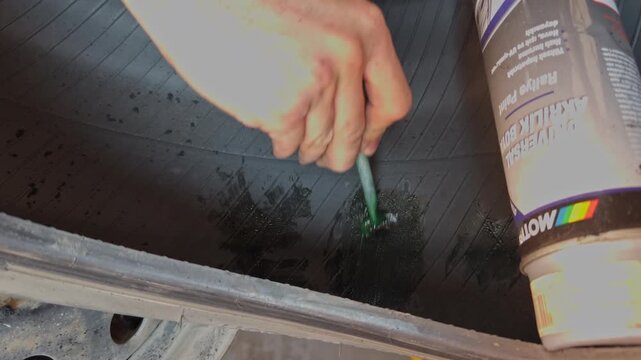 A hand applies black rubber cement with a brush onto the sanded puncture area inside a burst tire before attaching a repair patch