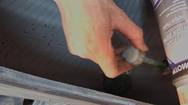 A hand brushes black rubber cement liquid into the puncture hole of the same tire in preparation for patching