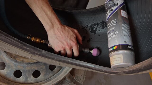 A hand uses a rotary sanding tool to flatten and smooth the puncture hole on a burst tire before patch repair