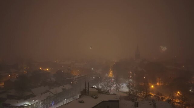 Aerial view of vibrant fireworks exploding over the snow-covered rooftops of Riga, Latvia.