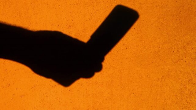 Close-up shadow silhouette of a hand using a flip dumb phone and texting.