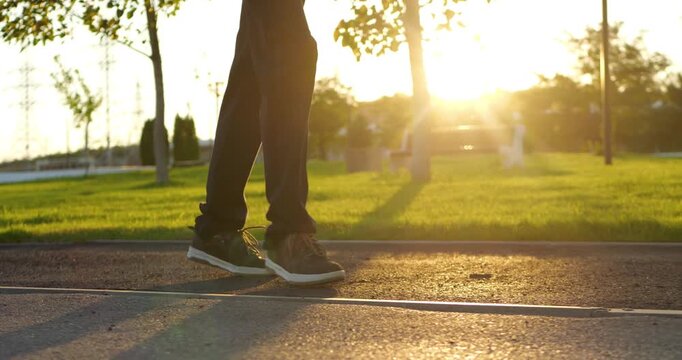 Teenage boy walks through sunlit park at golden hour. Close-up of legs and sneakers on paved path symbolizes independence, personal growth, freedom, youth and journey toward adulthood.