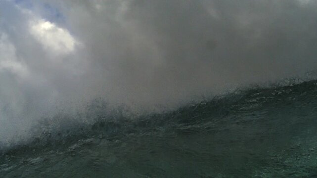 Breaking ocean wave surging beneath dense gray clouds and mist in extended slow motion