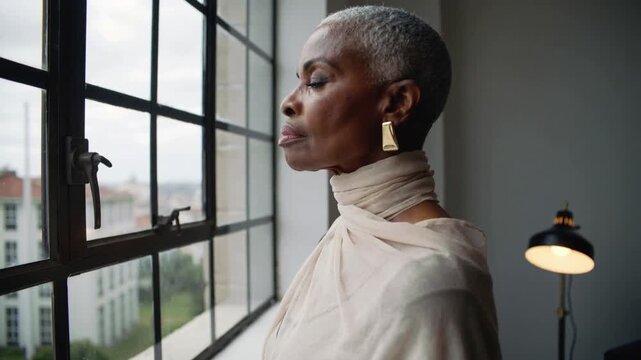 Breathing woman thinking in loft by window, scarf, earrings, lamp, camera rolling, copy space
