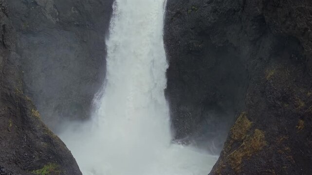 Powerful water stream of the Litlanesfoss waterfall plunging down a dramatic canyon framed by unique hexagonal basalt columns in Iceland